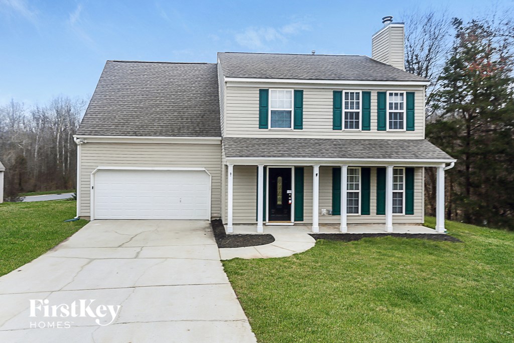 A house with a grey roof and green shutters is for sale.