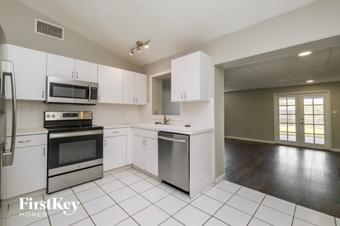 A kitchen with white cabinets and appliances, a dining table, and a large window.