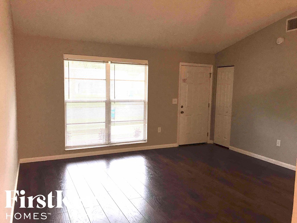 A room with wooden floors and a large window with blinds.