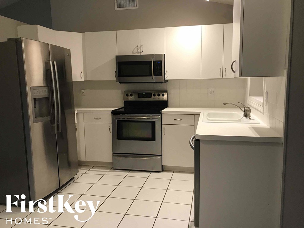 A kitchen with a refrigerator, microwave, oven, and sink.