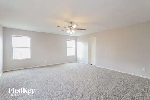 A spacious room with a ceiling fan and two windows.