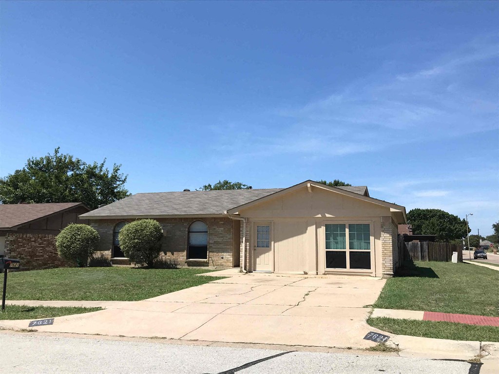 a small tan brick house with a driveway and grass