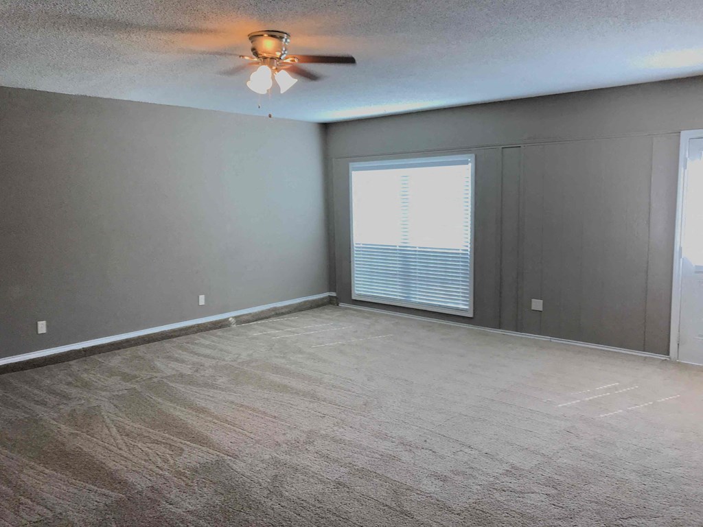 an empty living room with a ceiling fan and a window