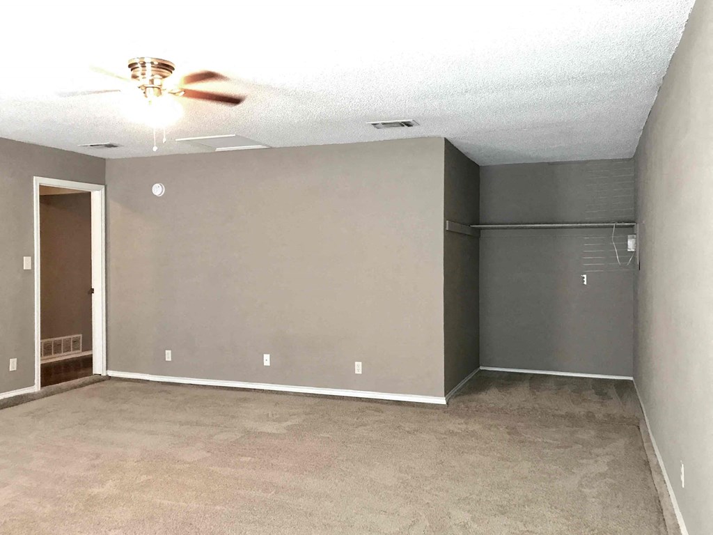 an empty living room with a ceiling fan and gray walls