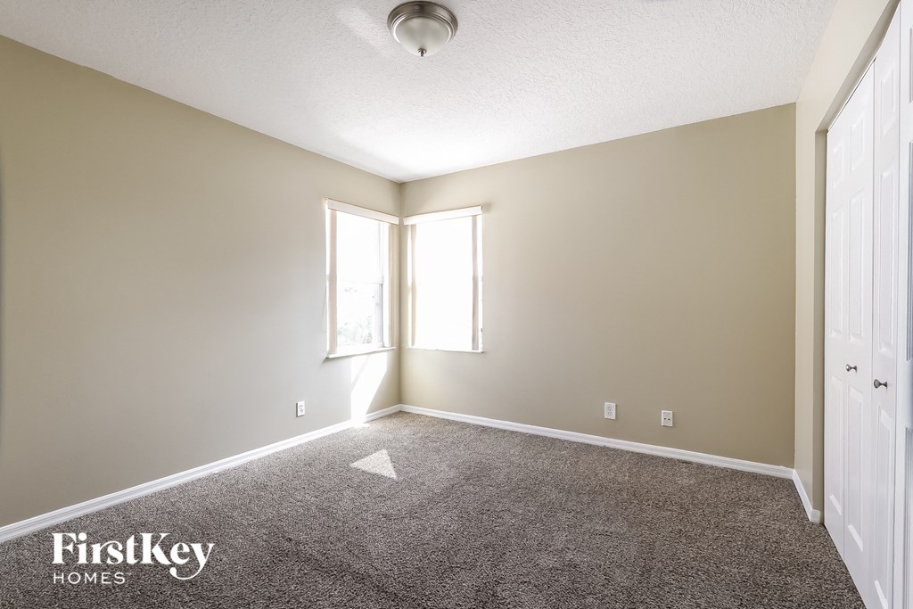 A room with a carpet floor, a white door, and a window with sunlight coming through.