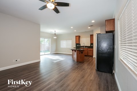 A spacious kitchen and living room with a black refrigerator and wooden floors.