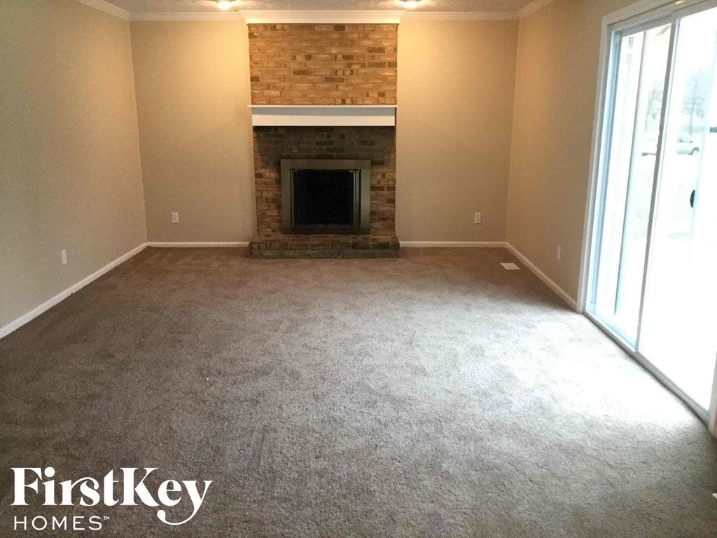 an empty living room with a fireplace and carpeted floor