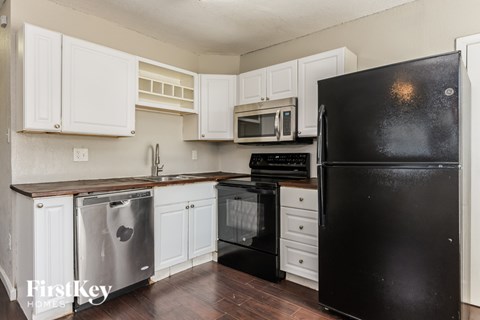 A black refrigerator is in the corner of a kitchen with white cabinets.
