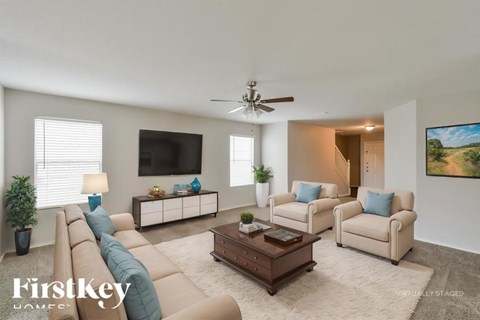 A living room with a beige sofa, two armchairs, a coffee table, and a flat-screen TV mounted on the wall.