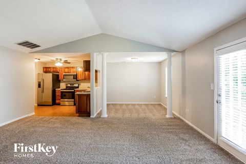 A spacious living room with a kitchen in the background and a carpet on the floor.