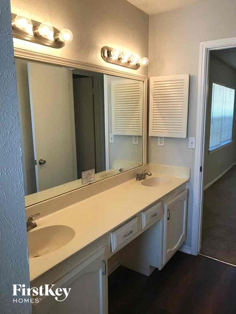 A bathroom with a white counter top and a mirror above it.
