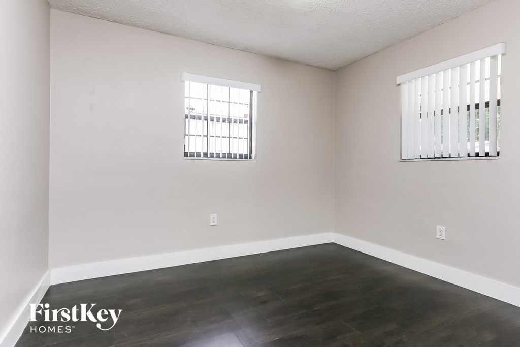 a living room with wood floors and white walls and two windows