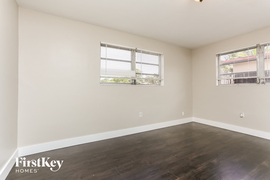 a living room with wood floors and white walls and two windows
