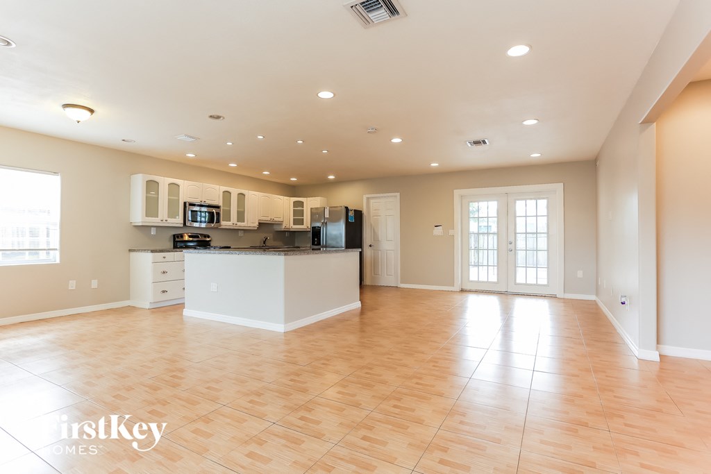 an empty living room with a kitchen and a window