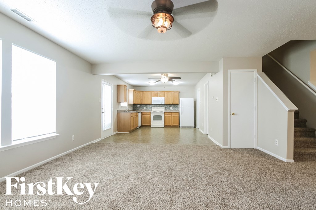 an empty living room with a ceiling fan and a kitchen