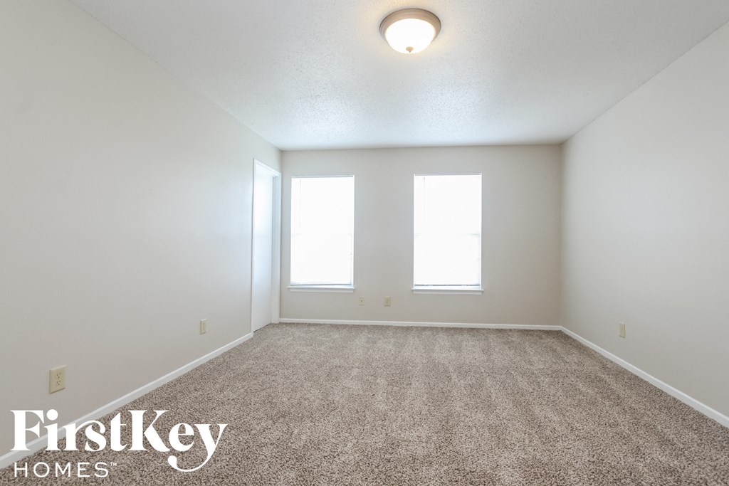 a spacious living room with carpet and two windows