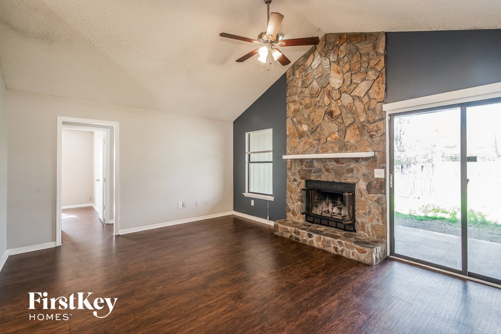 A spacious living room with a stone fireplace and a ceiling fan.