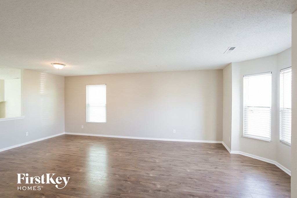 A spacious room with wooden flooring and two windows letting in natural light.