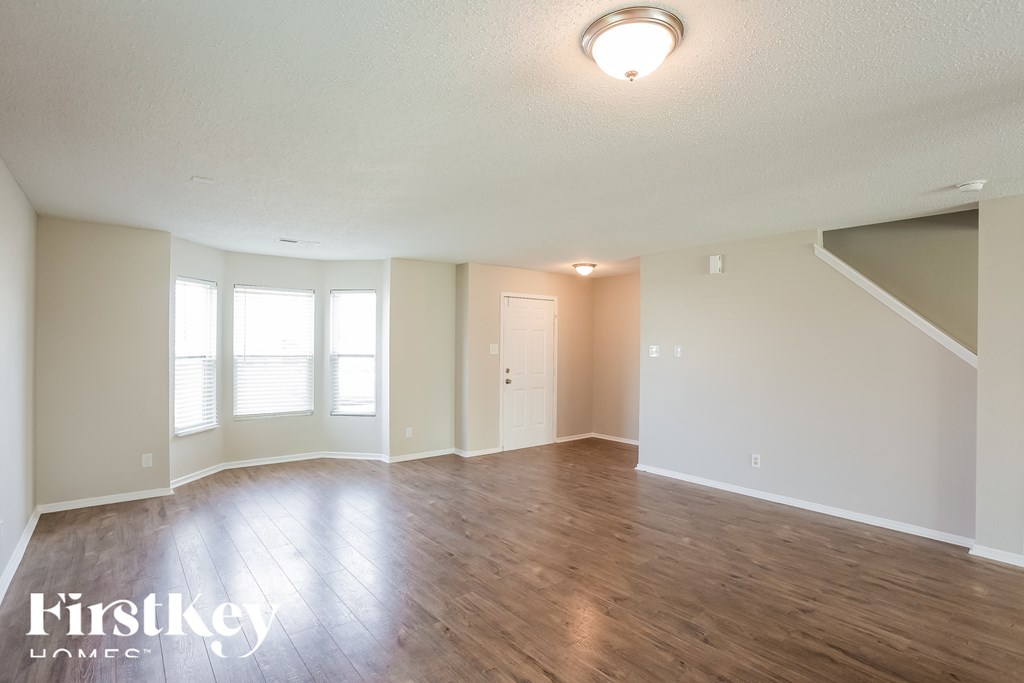 A spacious room with wooden floors and a staircase on the right.