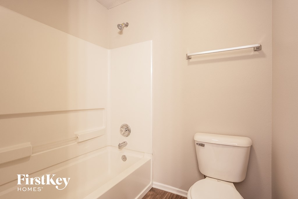 A white toilet in a small bathroom with a white tub and a white towel rack.