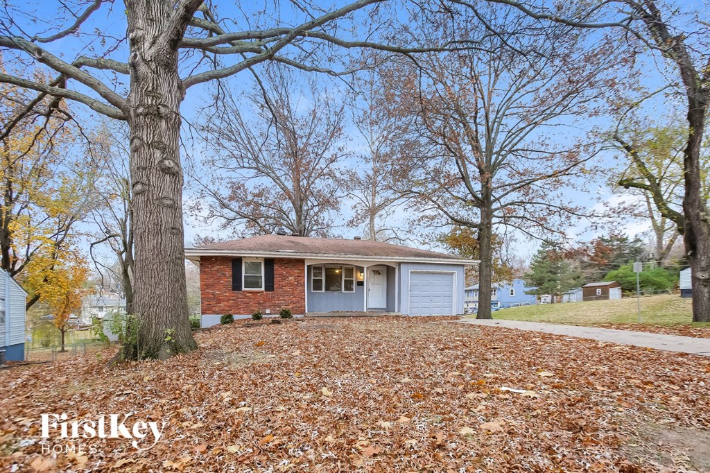 A house with a garage is surrounded by trees with yellow leaves.