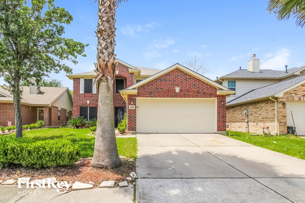A house with a red brick facade and a white garage door is for sale.