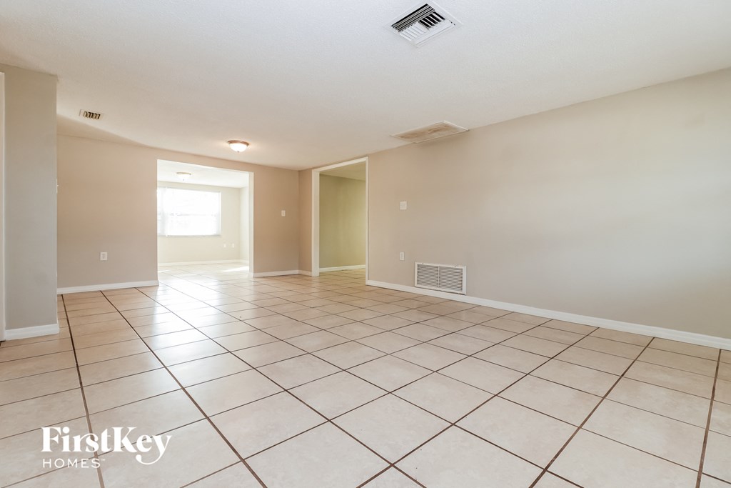 a spacious living room with tiled flooring and a door to the dining room