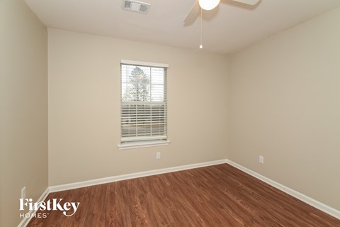 a bedroom with wood flooring and a window and a ceiling fan