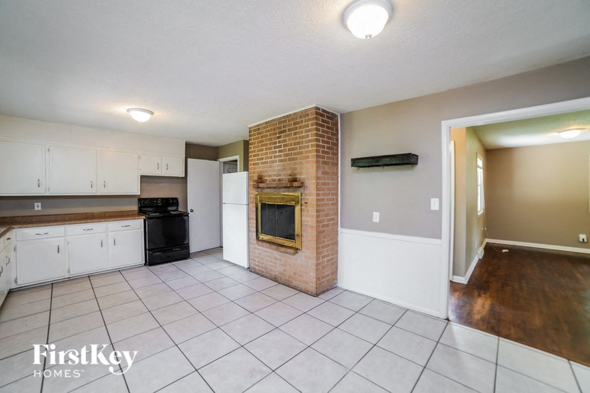 an empty kitchen with a brick fireplace and white cabinets