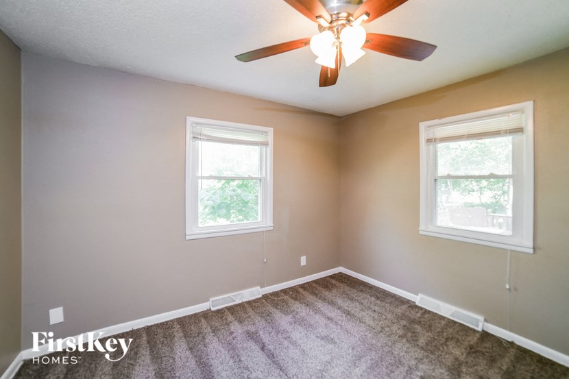 an empty bedroom with a ceiling fan and two windows