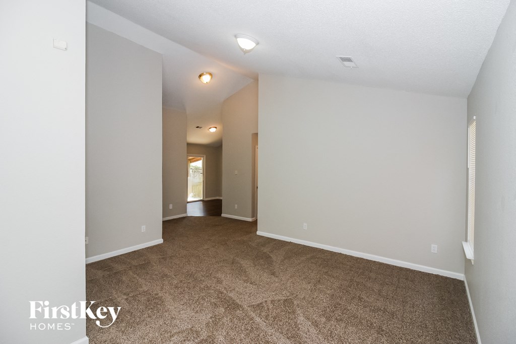 A spacious room with a carpeted floor and white walls, with a doorway leading to another room visible in the distance.