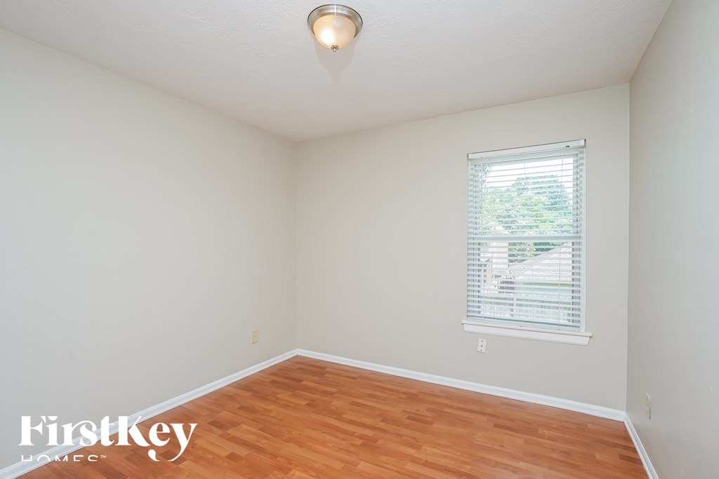 a bedroom with white walls and wood floors and a window