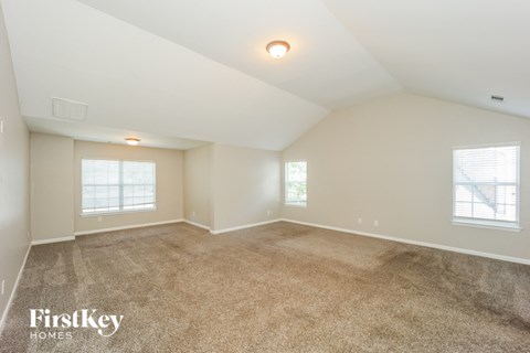 a spacious living room with carpet and two windows
