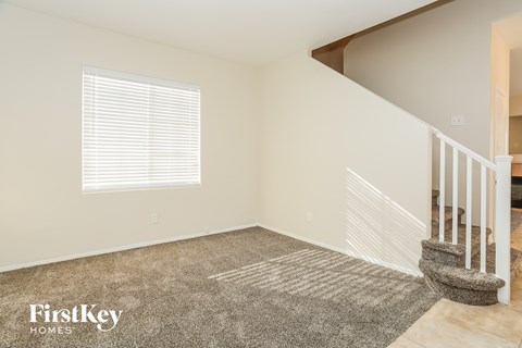 A room with a carpet, a window with blinds, and a staircase with a railing.