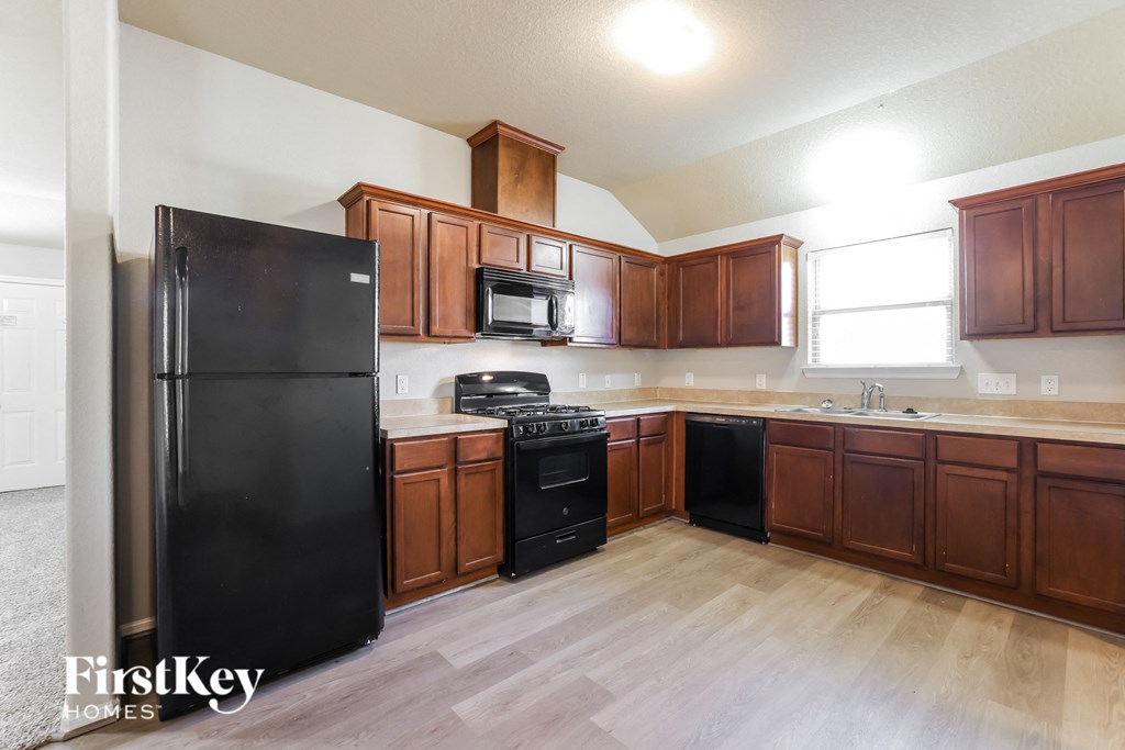 a kitchen with wood flooring and wooden cabinets and black appliances