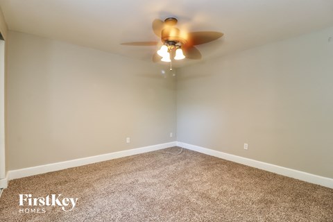 A carpeted room with a ceiling fan and a FirstKey Homes logo.