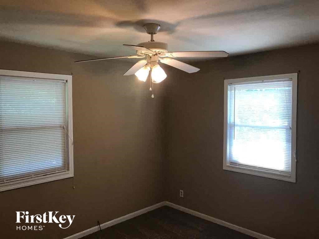 A room with a ceiling fan and two windows.