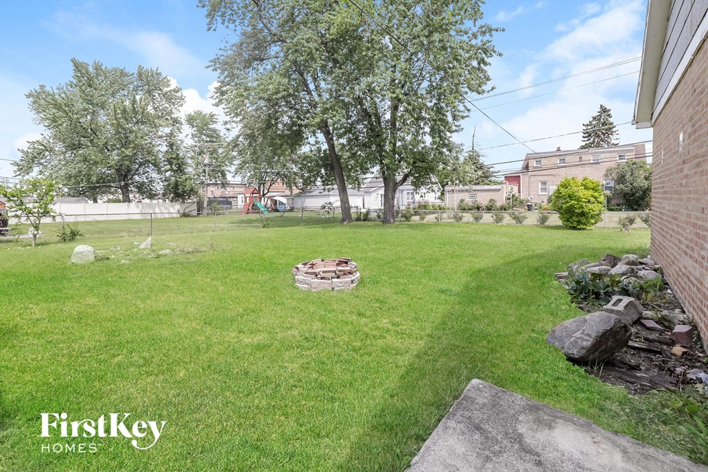 a backyard with green grass and a fire pit   and trees