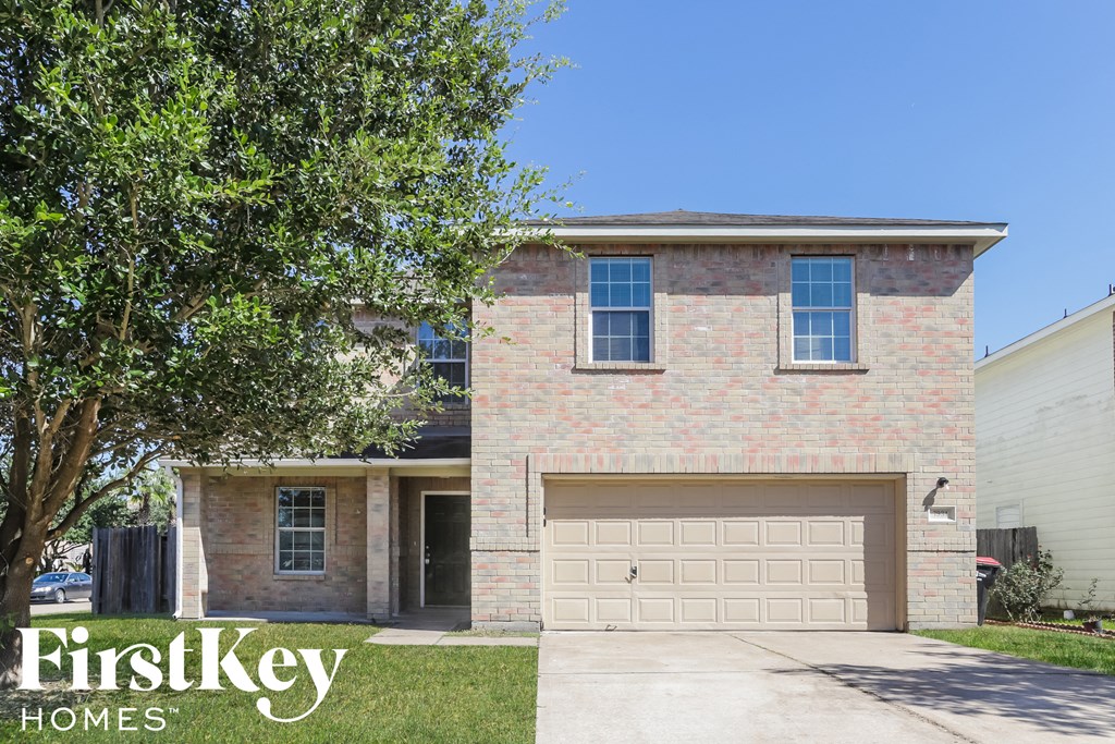 A brick house with a garage door and a tree in front.