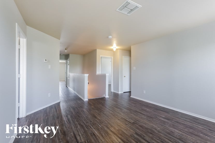 A spacious room with wooden floors and white walls, with a door on the left and a window on the right.