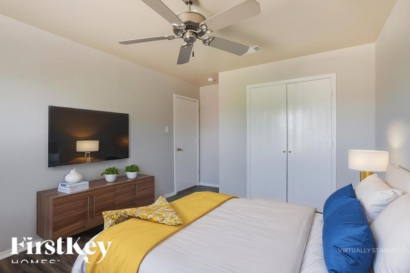 A bedroom with a bed, a ceiling fan, and a nightstand with a lamp.