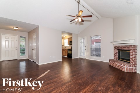 A spacious living room with wood flooring and a brick fireplace.