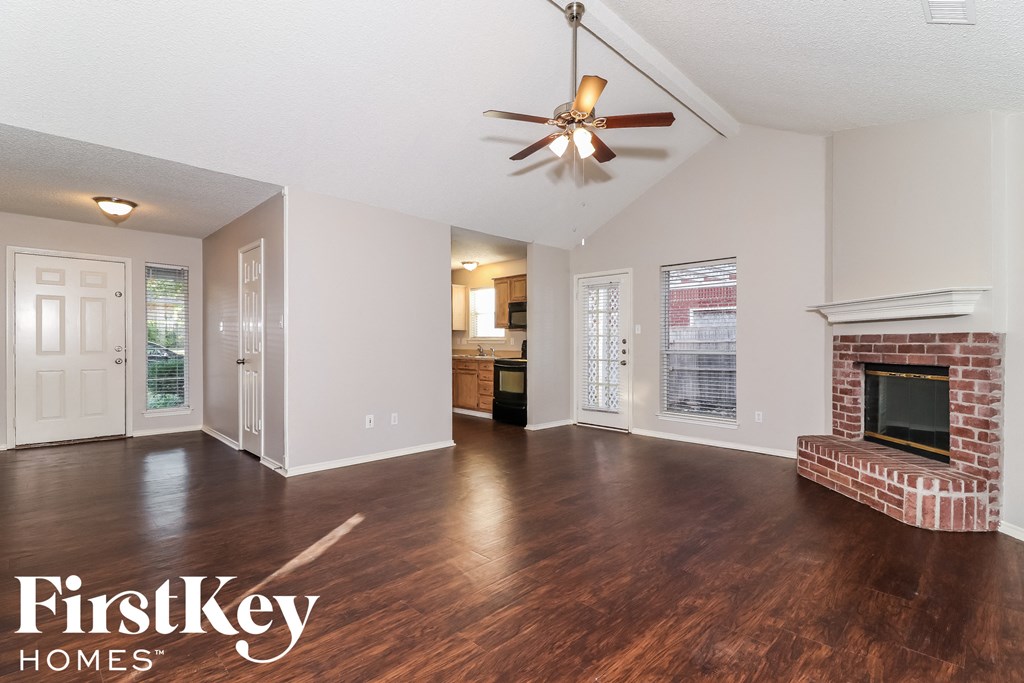 A spacious living room with wood flooring and a brick fireplace.