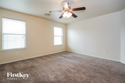 a carpeted living room with a ceiling fan and two windows