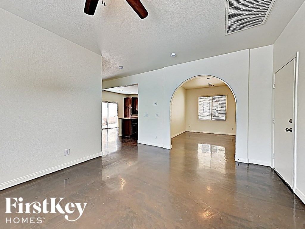 A spacious room with a fan and a doorway leading to another room.