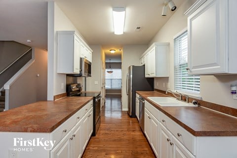 a kitchen with white cabinets and wood counter tops and a long hallway with a sink