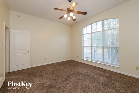 A room with a carpet floor, a ceiling fan, and a large window with a view of trees.