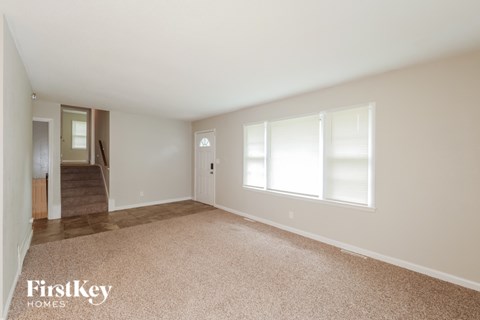 A spacious empty room with a carpeted floor and a staircase leading to another room.
