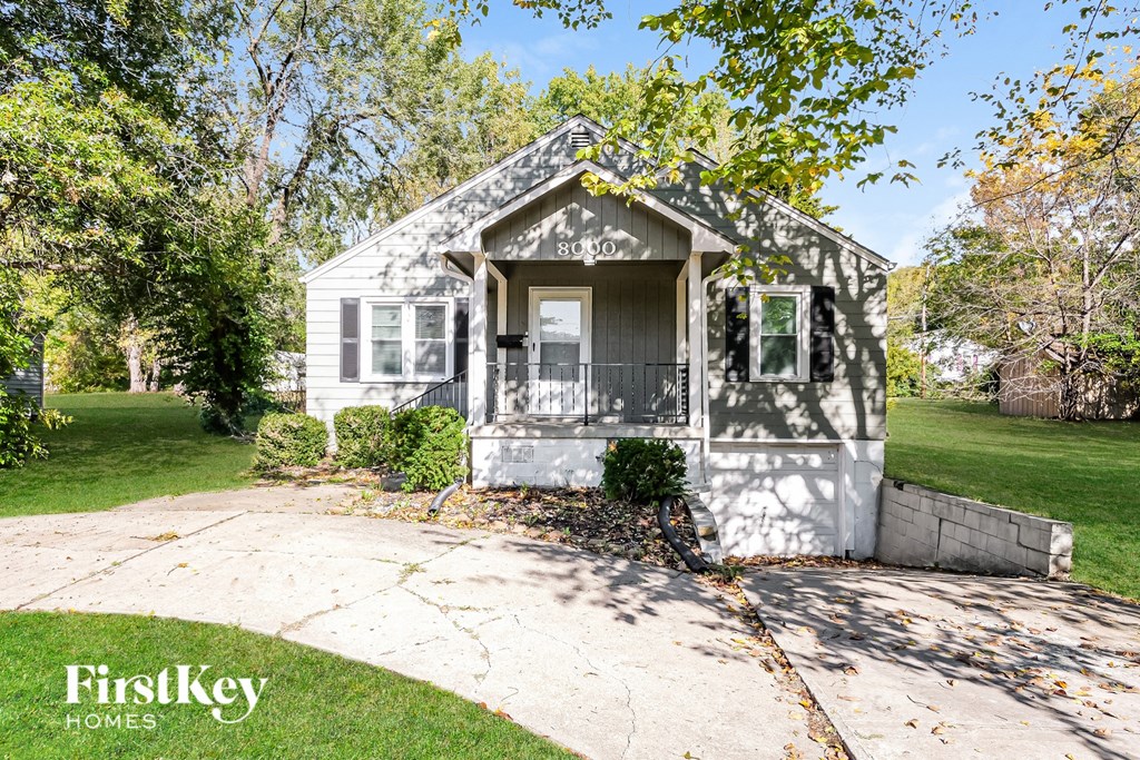 A small house with a porch is surrounded by trees.