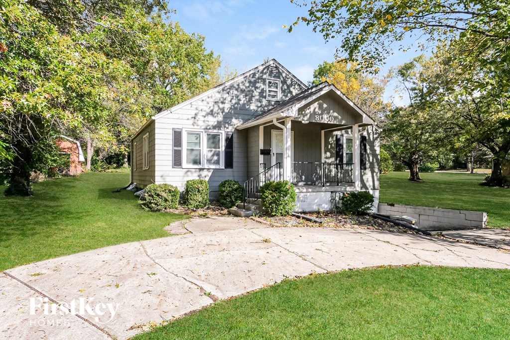 A small house with a porch is surrounded by a green lawn.